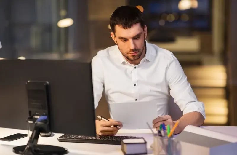 Empresario revisando documentos sobre cliente tóxico por la noche en la oficina